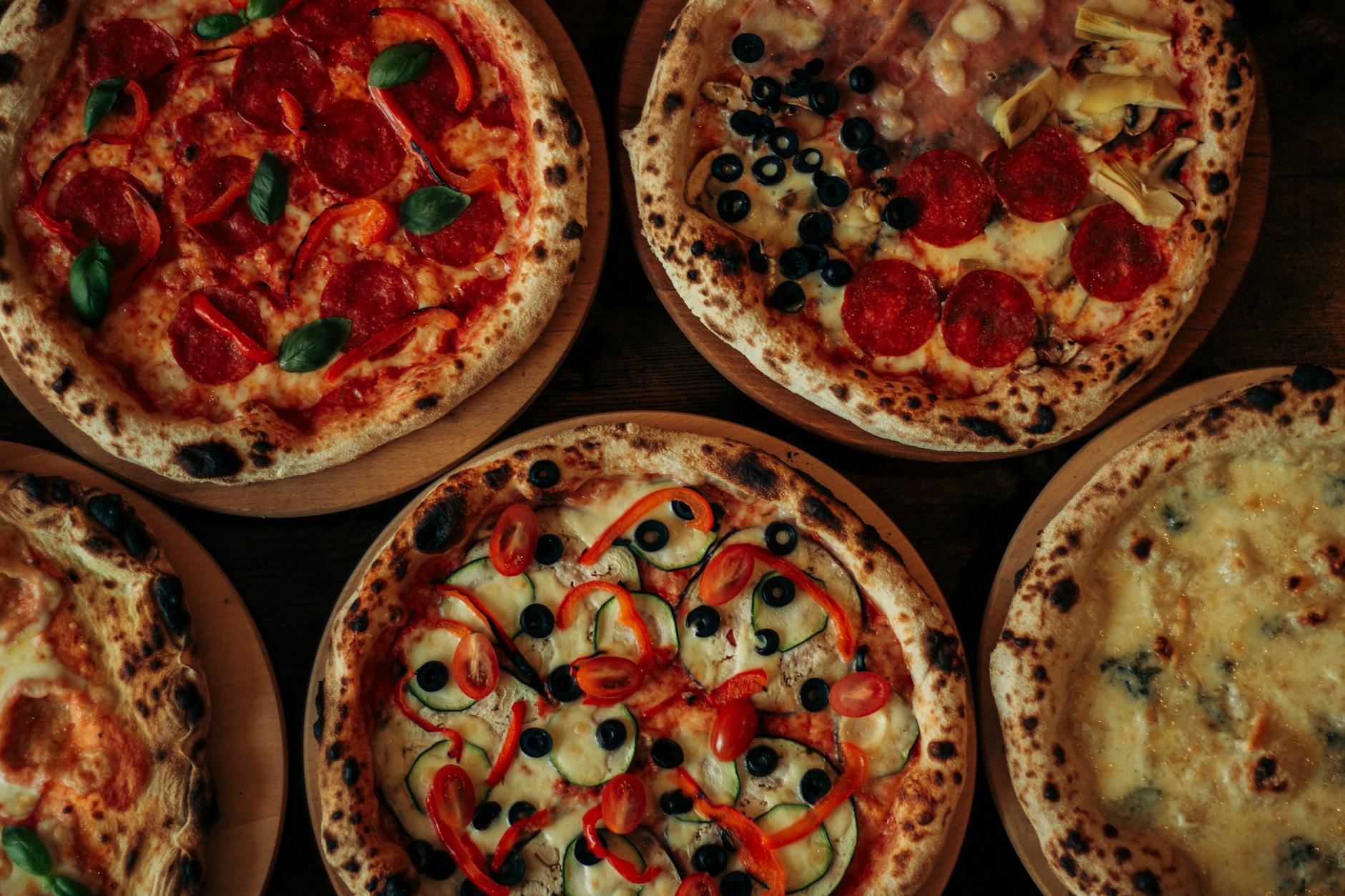 Różne pizze gourmet na drewnianych deskach z kolorowymi dodatkami