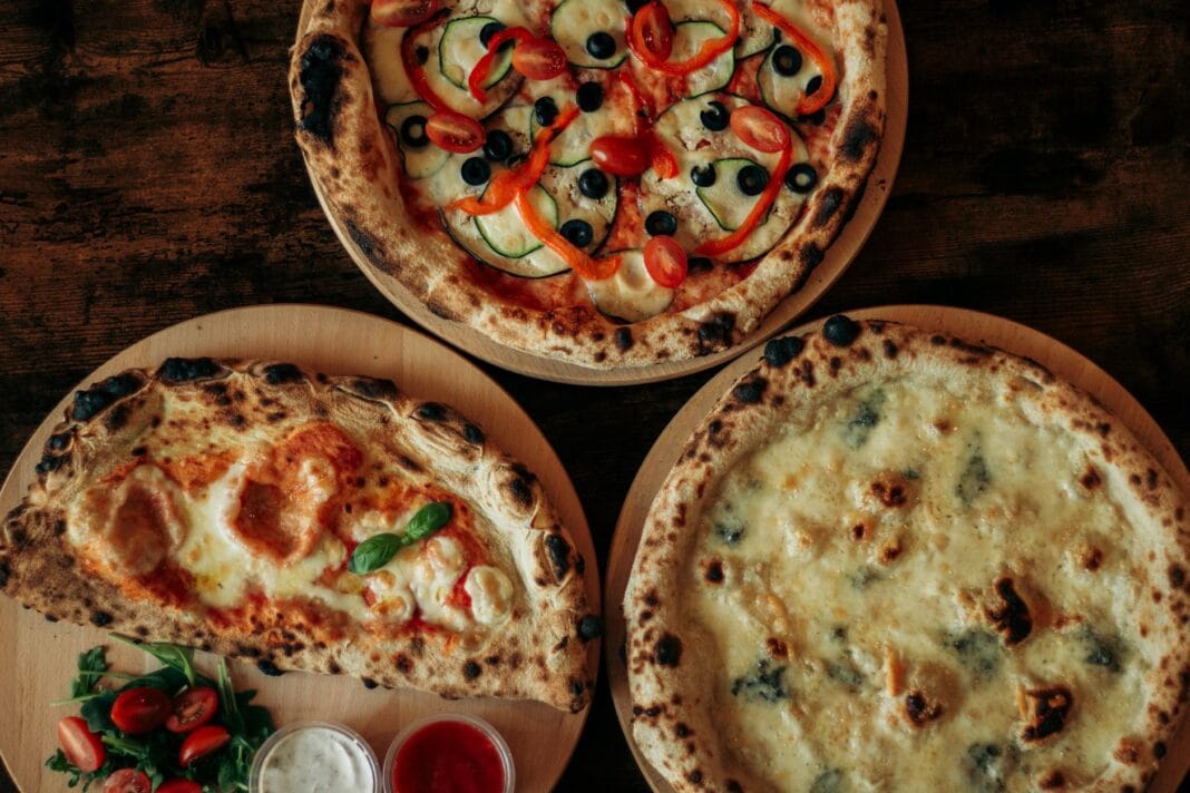 Trzy pizze z różnymi serami i dodatkami na drewnianych deskach widziane z góry