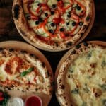 Trzy pizze z różnymi serami i dodatkami na drewnianych deskach widziane z góry