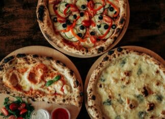 Trzy pizze z różnymi serami i dodatkami na drewnianych deskach widziane z góry