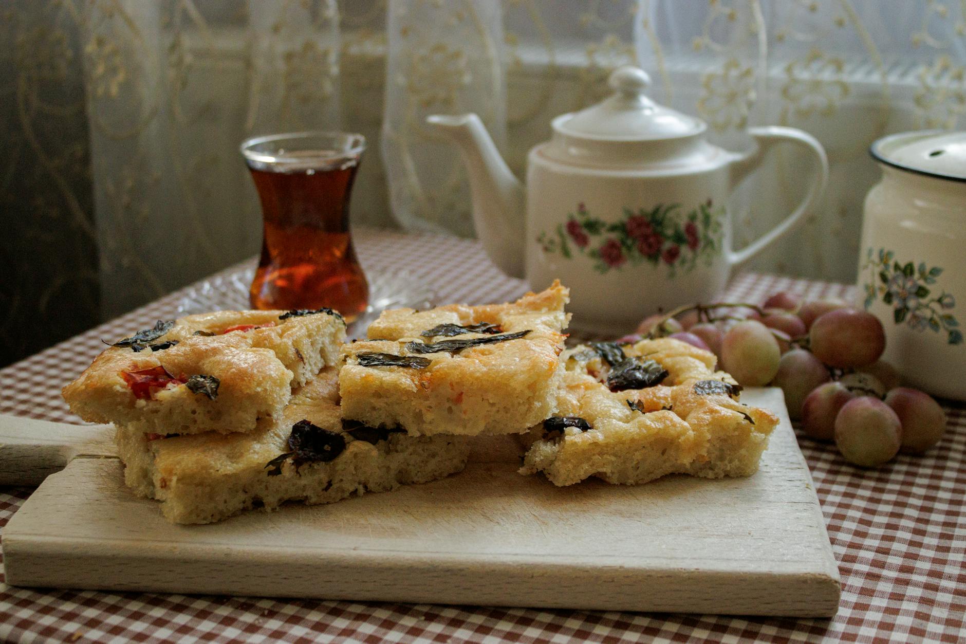 Rustykalna focaccia z oliwkami na desce obok herbaty i winogron