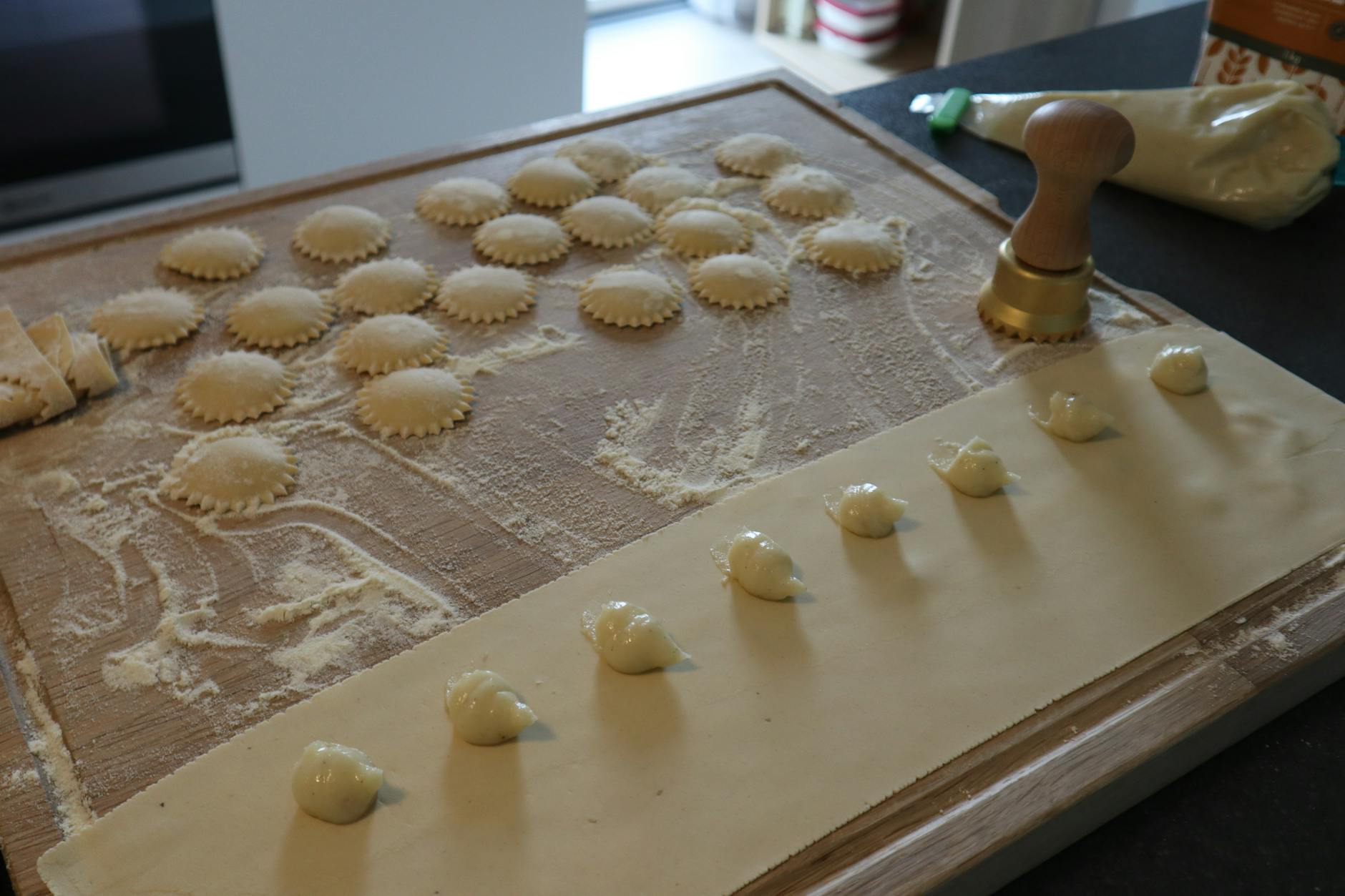 Świeże ravioli na oprószonej mąką desce obok stempelka do makaronu
