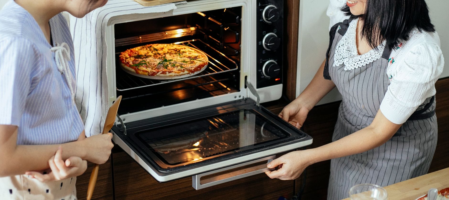 Sekrety pieczenia pizzy w małych piekarnikach i kuchenkach wolnostojących Kobieta w kuchni wkłada domową pizzę do małego piekarnika elektrycznego