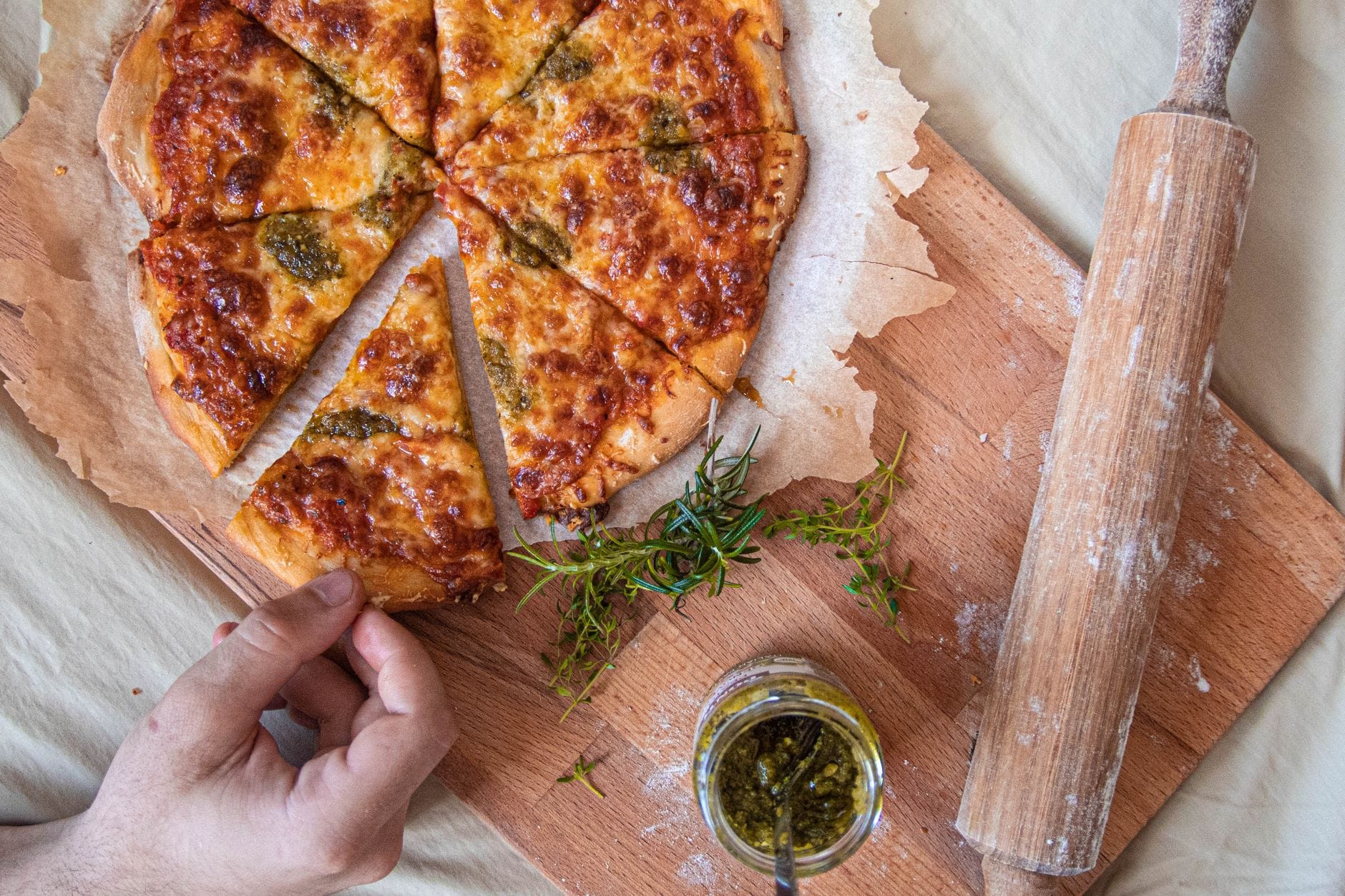 Dłoń sięga po kawałek domowej pizzy z ziołami na drewnianej desce