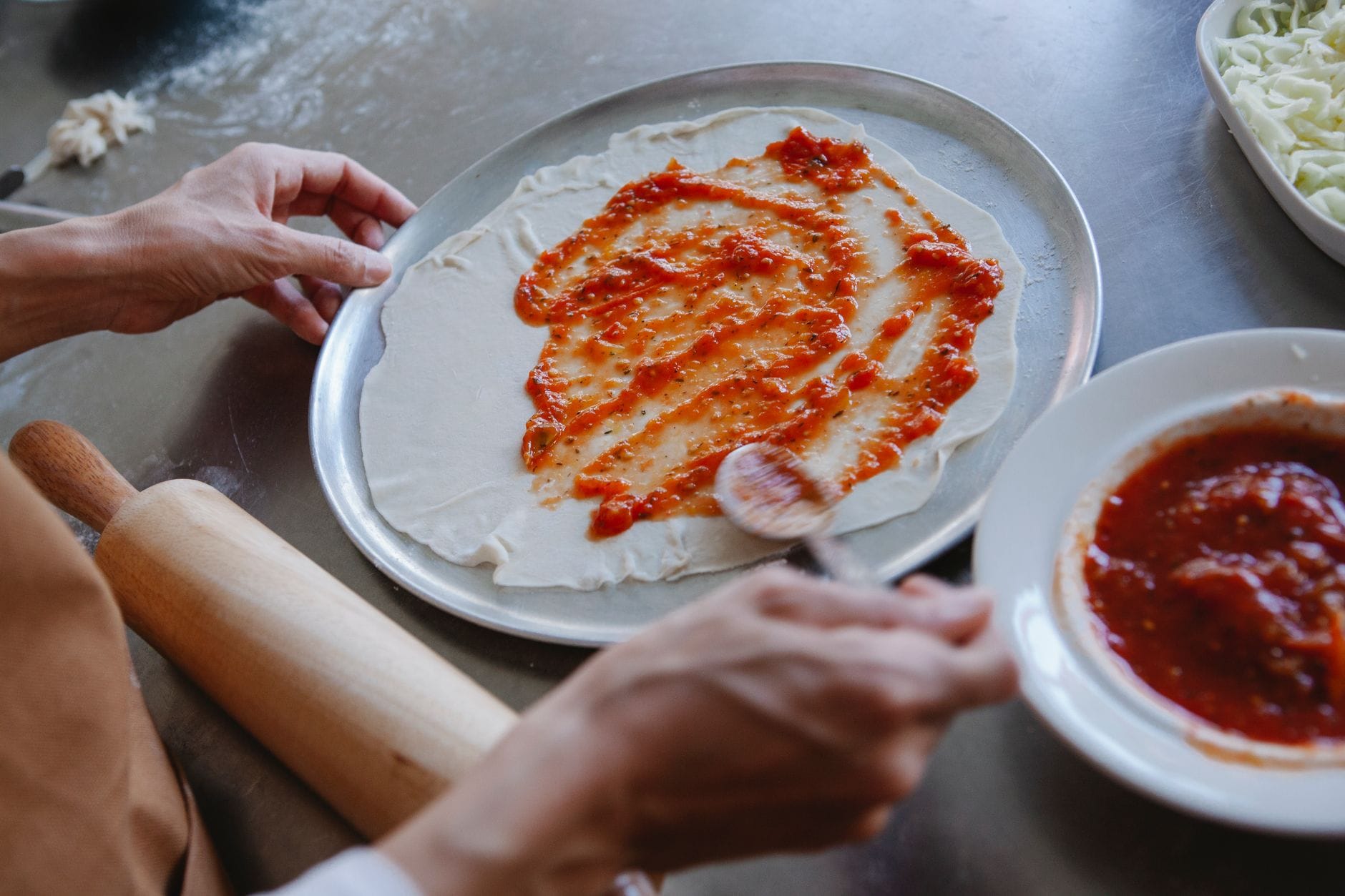 Rozsmarowywanie gęstego sosu pomidorowego na cieście do pizzy Rozsmarowywanie gęstego sosu pomidorowego na cieście do pizzy