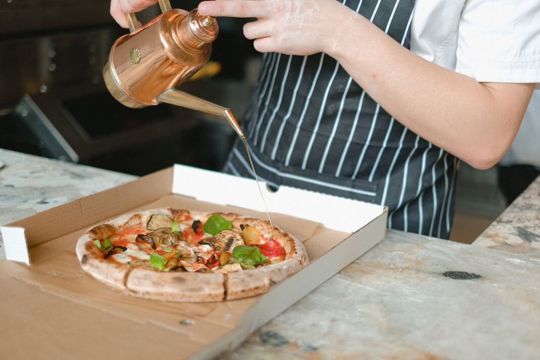 Kucharz polewa świeżą pizzę oliwą w kuchni pizzerii Kucharz polewa świeżą pizzę oliwą w kuchni pizzerii