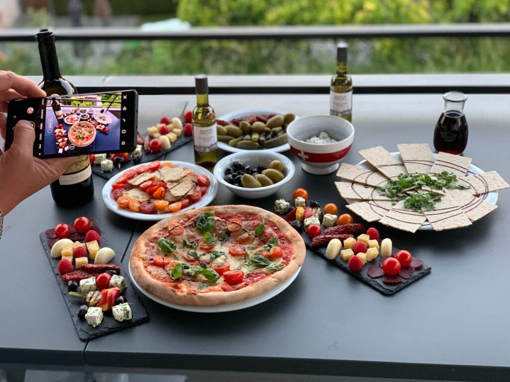 Osoba fotografuje pizzę na stole w ogródku restauracyjnym